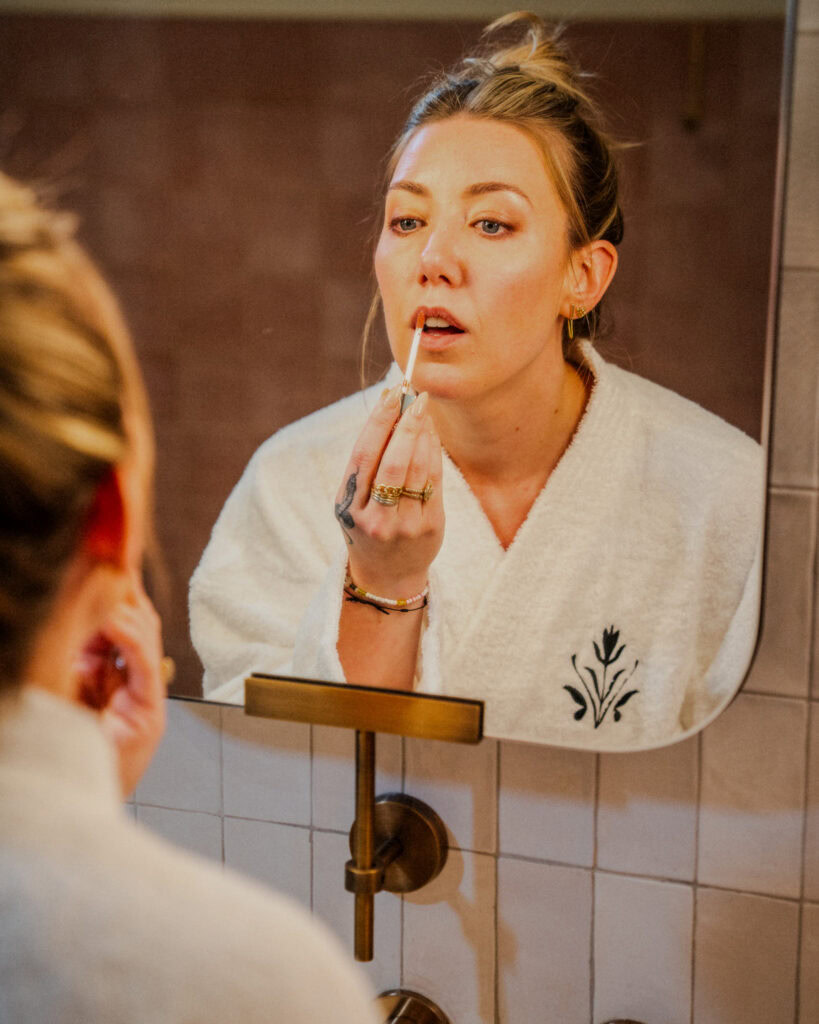 A woman at The Village community applying lipstick in front of a mirror.