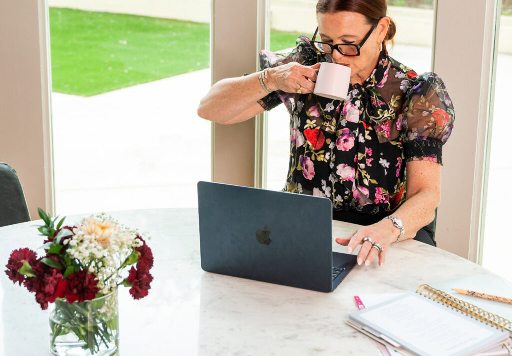 Woman working on laptop and drinking coffee at home.
